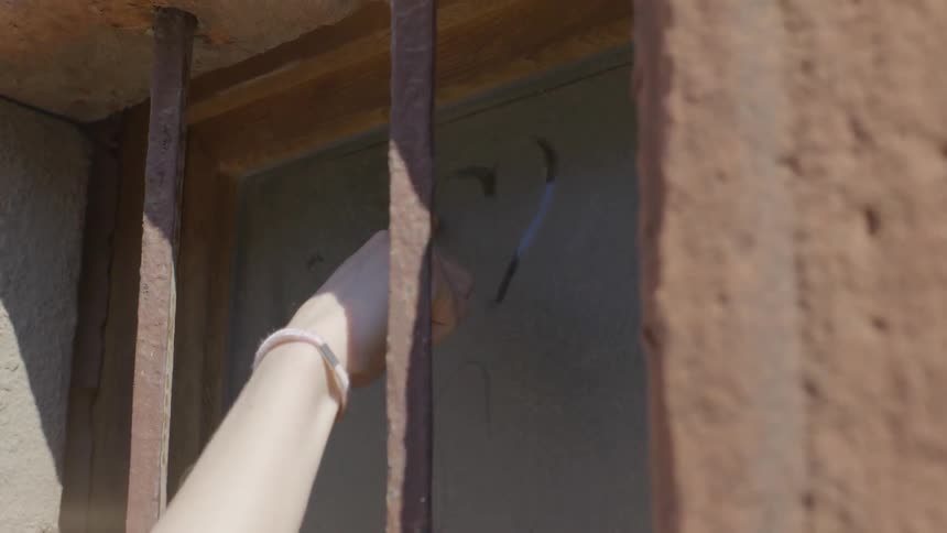A woman is tracing a heart on a dirty window outside a building during the day