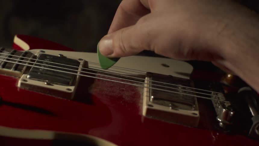 A man strikes the strings of a red electric guitar with a pick