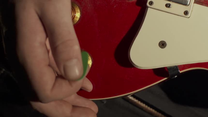 Someone is holding a guitar and pick close up