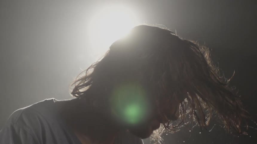 Man swings his wet hair around in front of a flood light