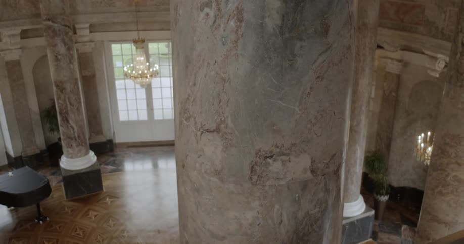Chandeliers light the interior of a rotunda room with marble columns and floor