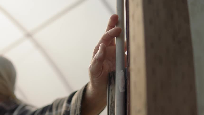 A man grips a pipe in a greenhouse