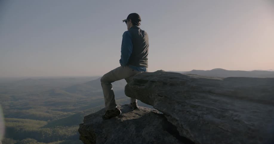 Man sits on a rock overlooking hilly land