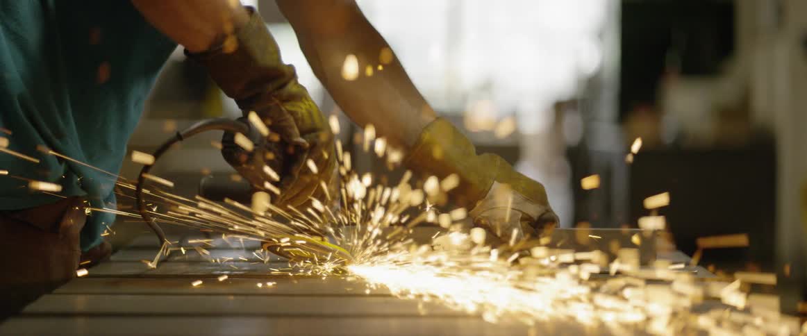 A man uses a grinder on a steel rod