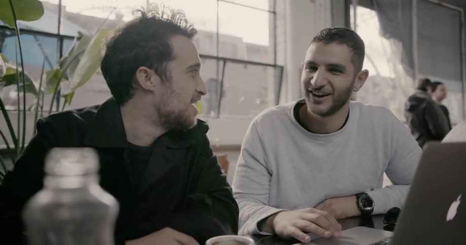 Two men smile while looking at a laptop
