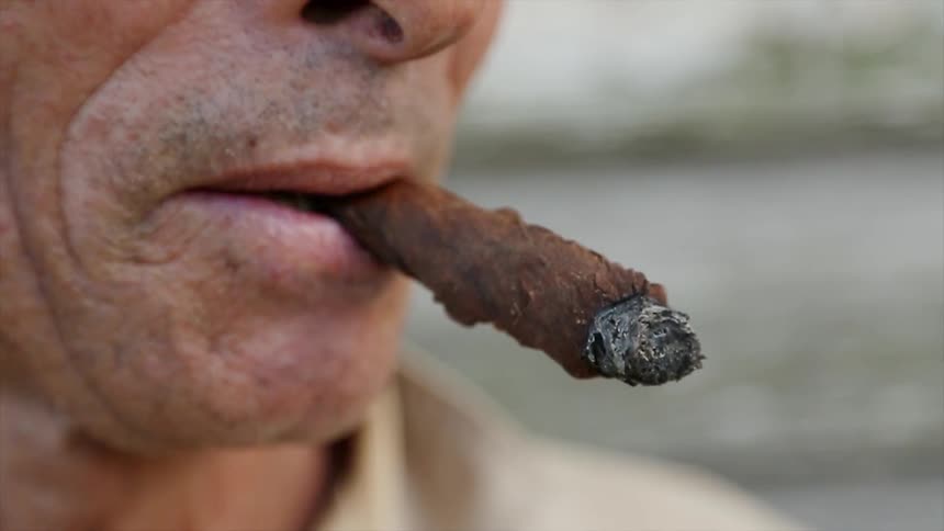 A man is smoking a cigar outside during the day
