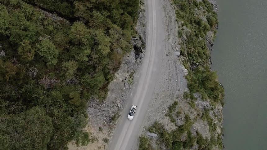 A vehicle travels down a mountain road next to water