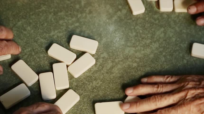 A group of men grab dominoes off a table
