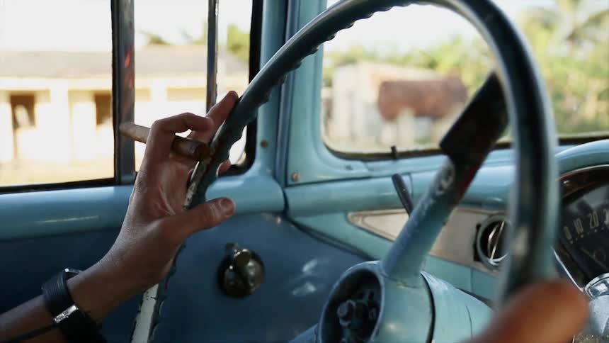 A person with a cigar in one hand drives a truck