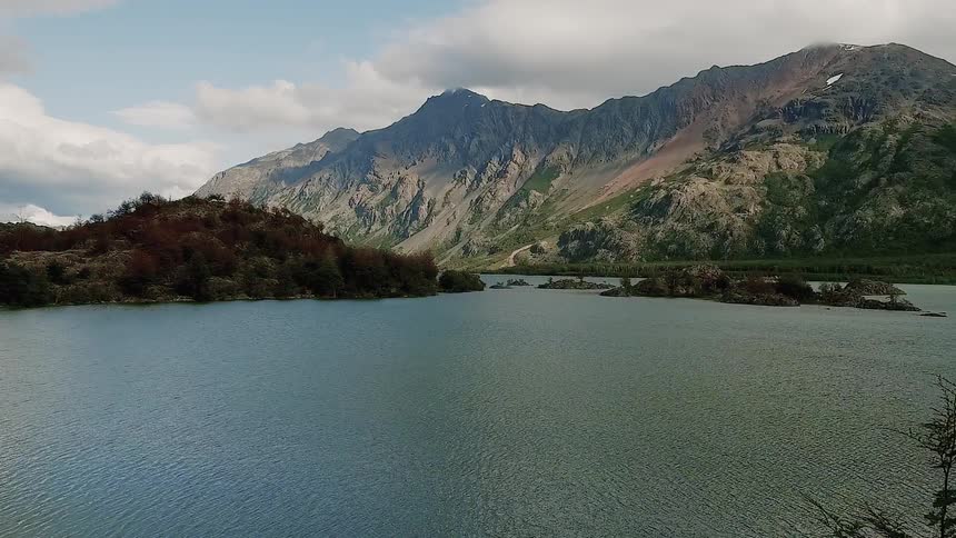 The drone flies out over a lake with a mountain in the background