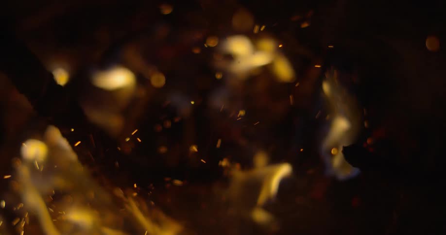 A stick being poked into a burning bonfire is stirring up sparks and ash