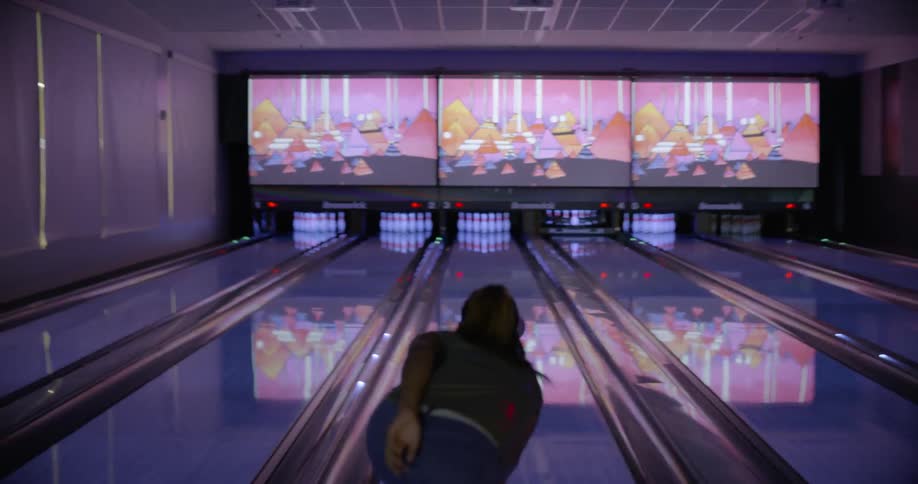 Woman rolls a bowling ball down a lane