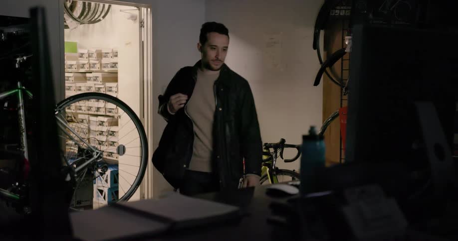 A man rolls his bike into a shop and walks over to the computer