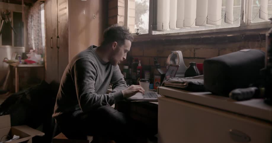 A man is sitting at a table looking at his laptop