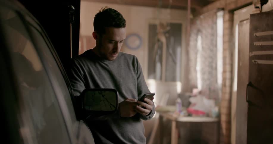 A man leans against a car looking at his phone