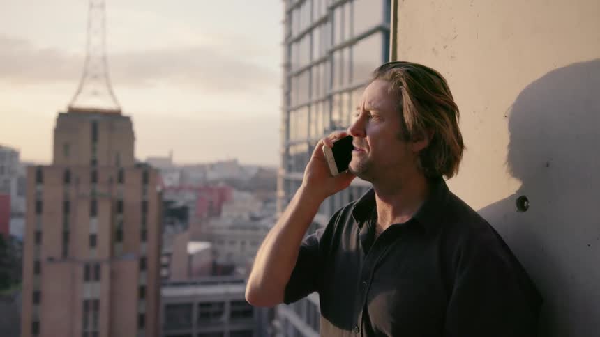 A man is standing on a balcony talking to someone on his phone
