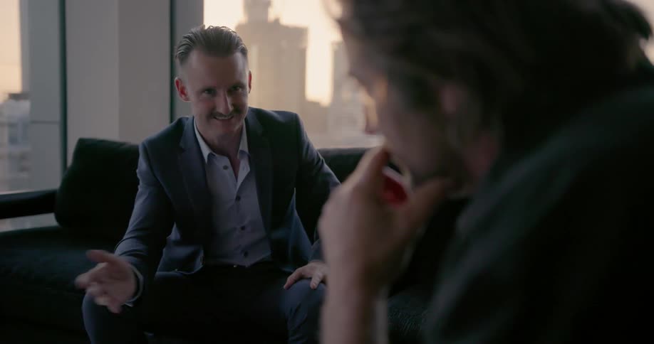 Two men are sitting on a couch talking to each other