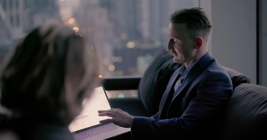 A man talks to another man while using his laptop
