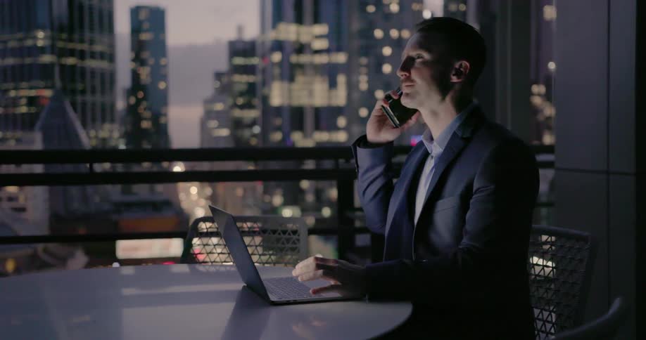 Man types on a laptop on a city balcony