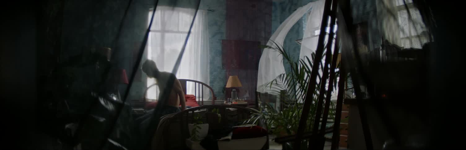 Man sitting up in bedroom behind a curtain