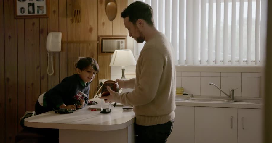 A young boy sits at a counter as a man makes coffee