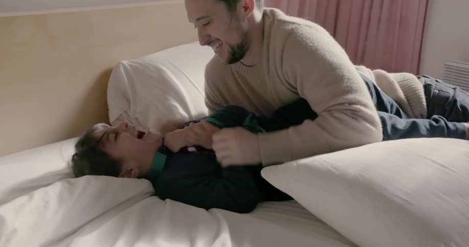 A man tickles his child in bed
