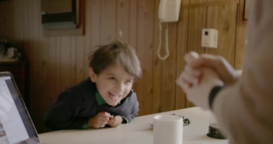 A child laughs as a woman talks to him at the kitchen bench