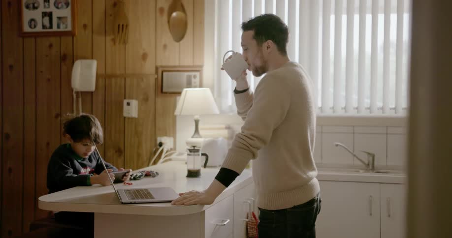Man sips from mug while looking at laptop in kitchen