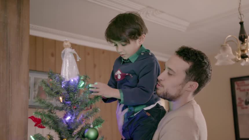 A little boy is putting the bell on the Christmas tree