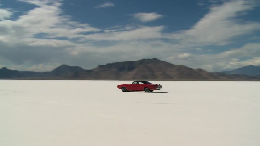 A red classic car is driving across the salt flats