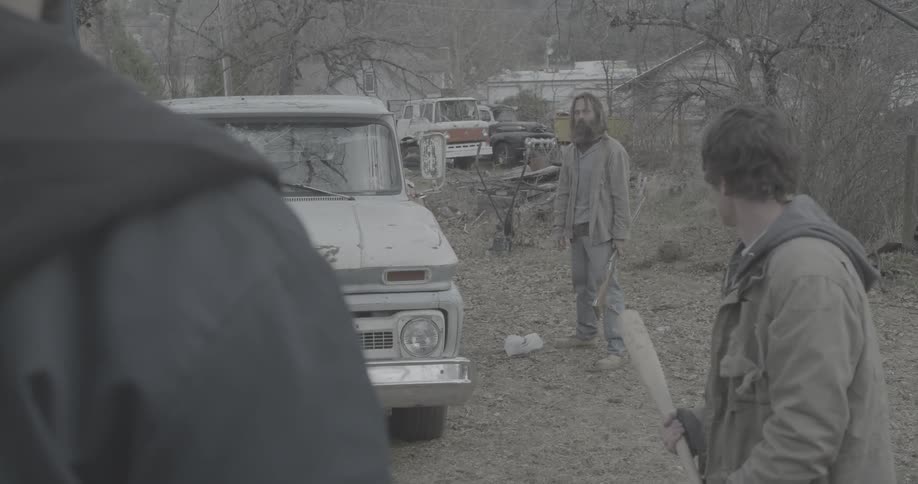 Man standing next to a truck aim a gun at another person then lowers it