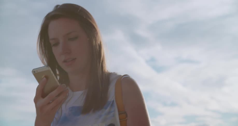 A woman is talking on her cellphone while walking outside during the day