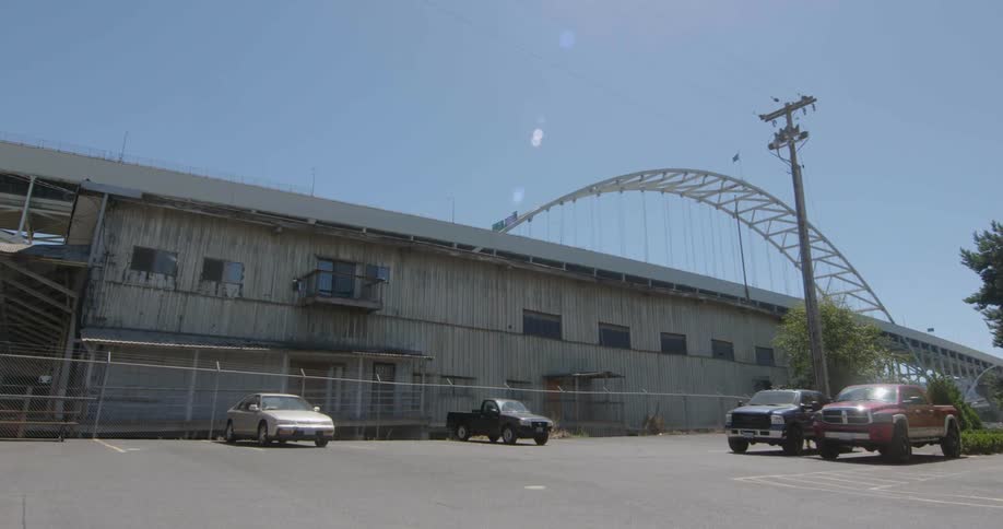 A car lot with a bridge in the background is filmed from the ground