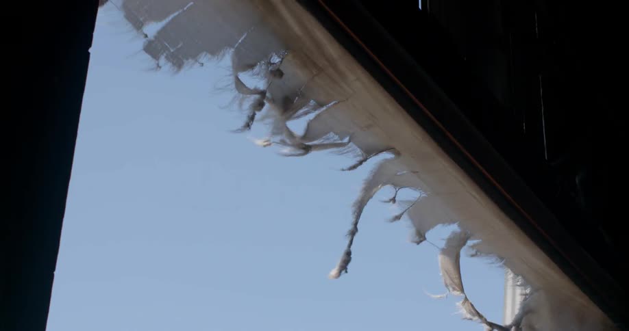 A torn canvas is swaying in the breeze above a doorway