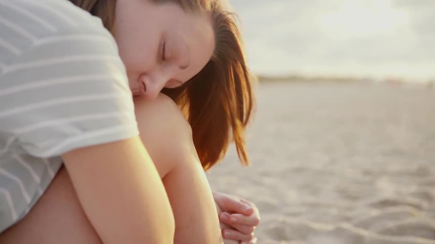 Woman sits with her head on her knees on the sand