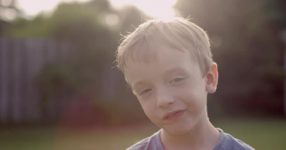 A boy smiles standing in his yard