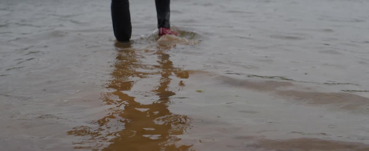 A man is walking into a river with pants and shoes on