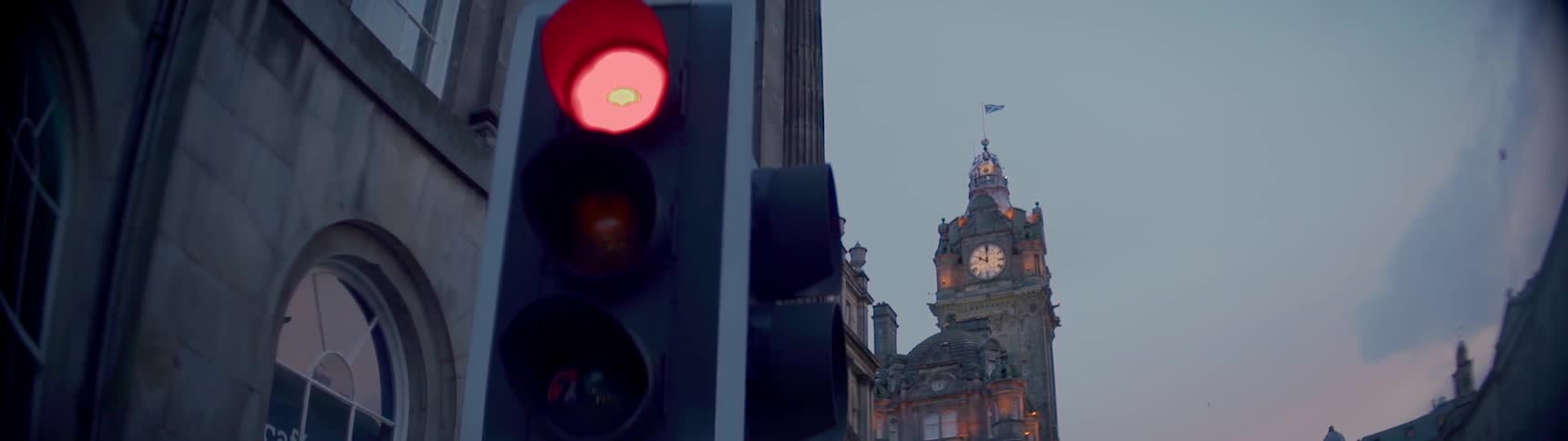 A clock tower in the background and a traffic light in the foreground