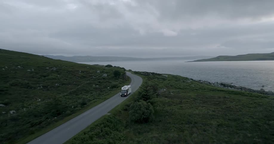 A camper truck is travelling down a winding road next to a large body of water