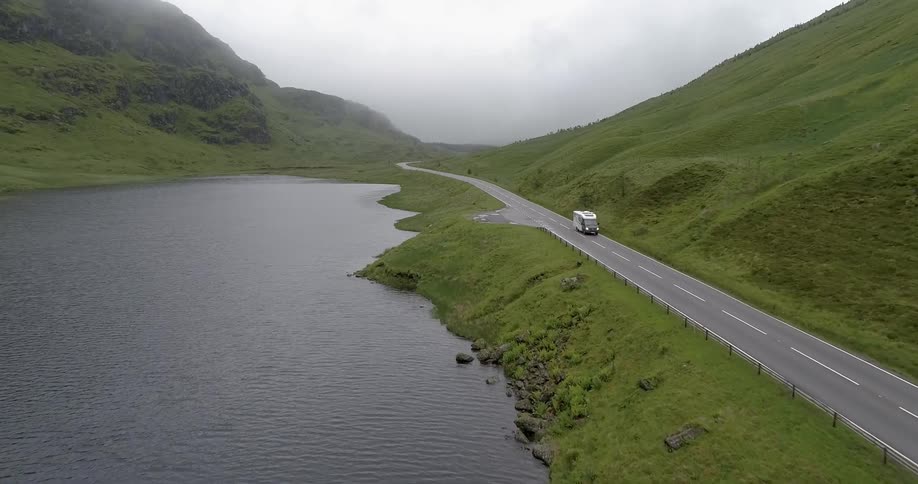 A vehicle drives on a mountain road near a lake