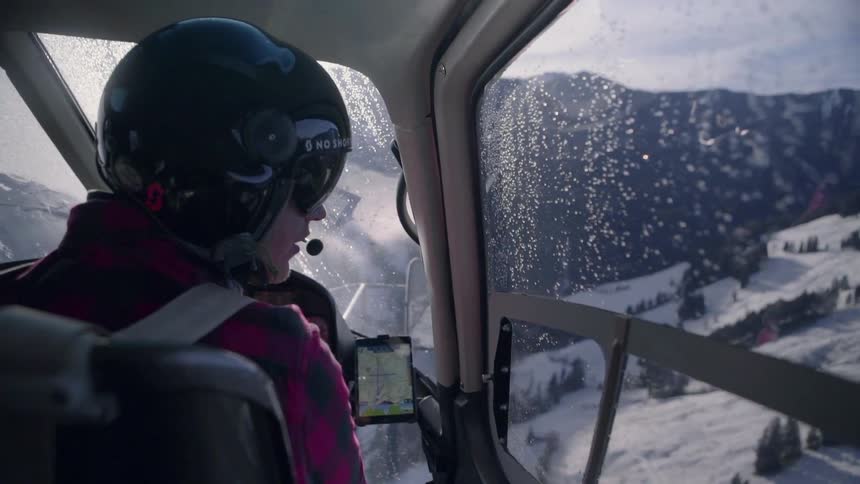 A pilot flies a helicopter over snowy mountains