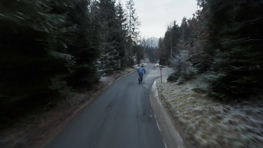 A bicyclist completes a wheelie as he rides on a country road in winter