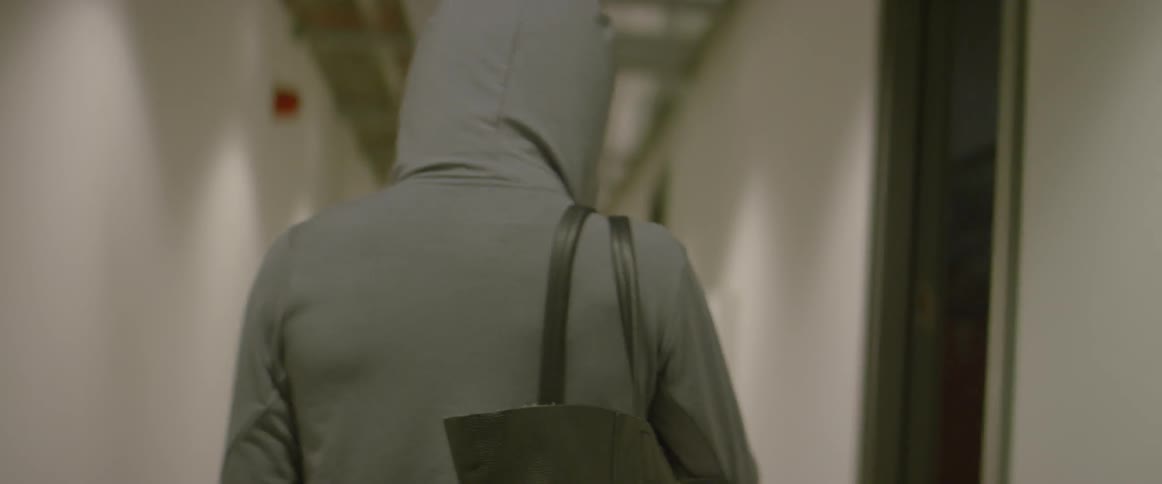 Woman holds tote bag and walks down a hall