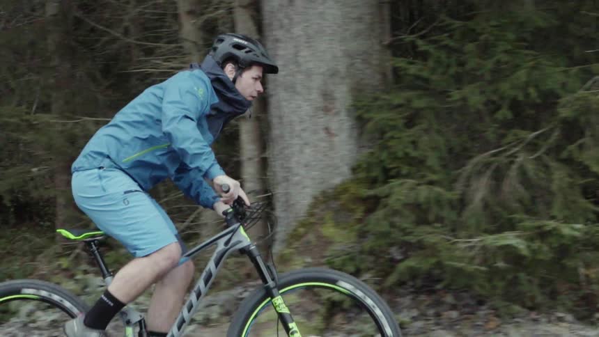 A man is riding a bicycle on a forest trail during the day