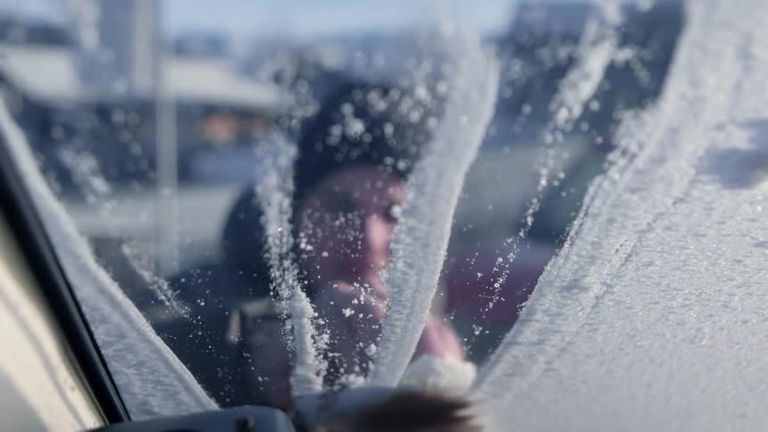 A man wipes snow off of a windshield