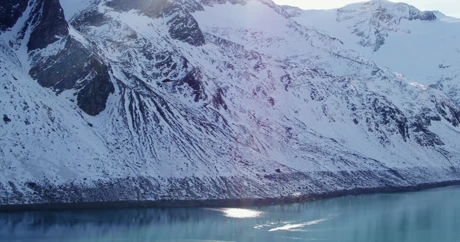 A helicopter is flying over a lake next to a snow covered mountain