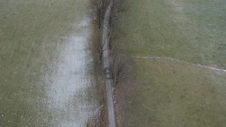 A car is traveling down a small road that's got two big pastures on either side