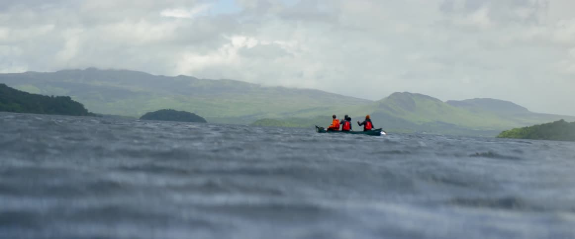 Three people are paddling a boat across a body of water