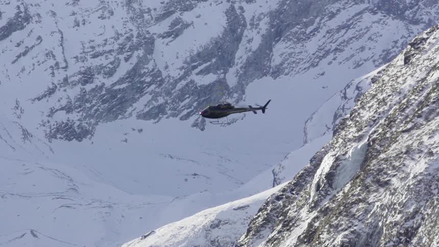 A helicopter flies above mountains