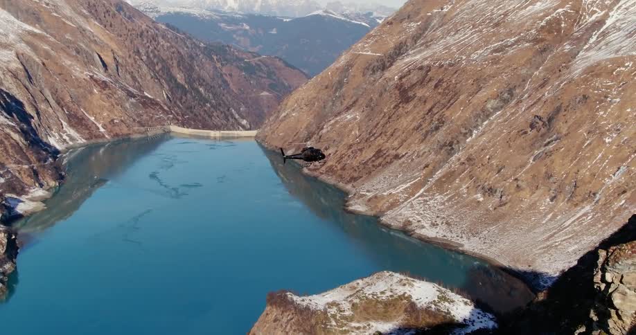A helicopter flies between mountains over a valley